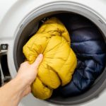 a hand placing hiking gear in a washing machine