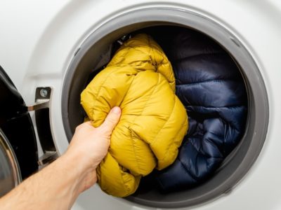 a hand placing hiking gear in a washing machine