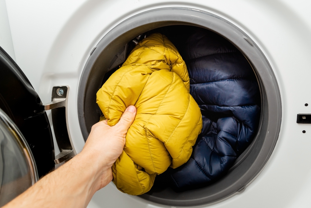 a hand placing hiking gear in a washing machine